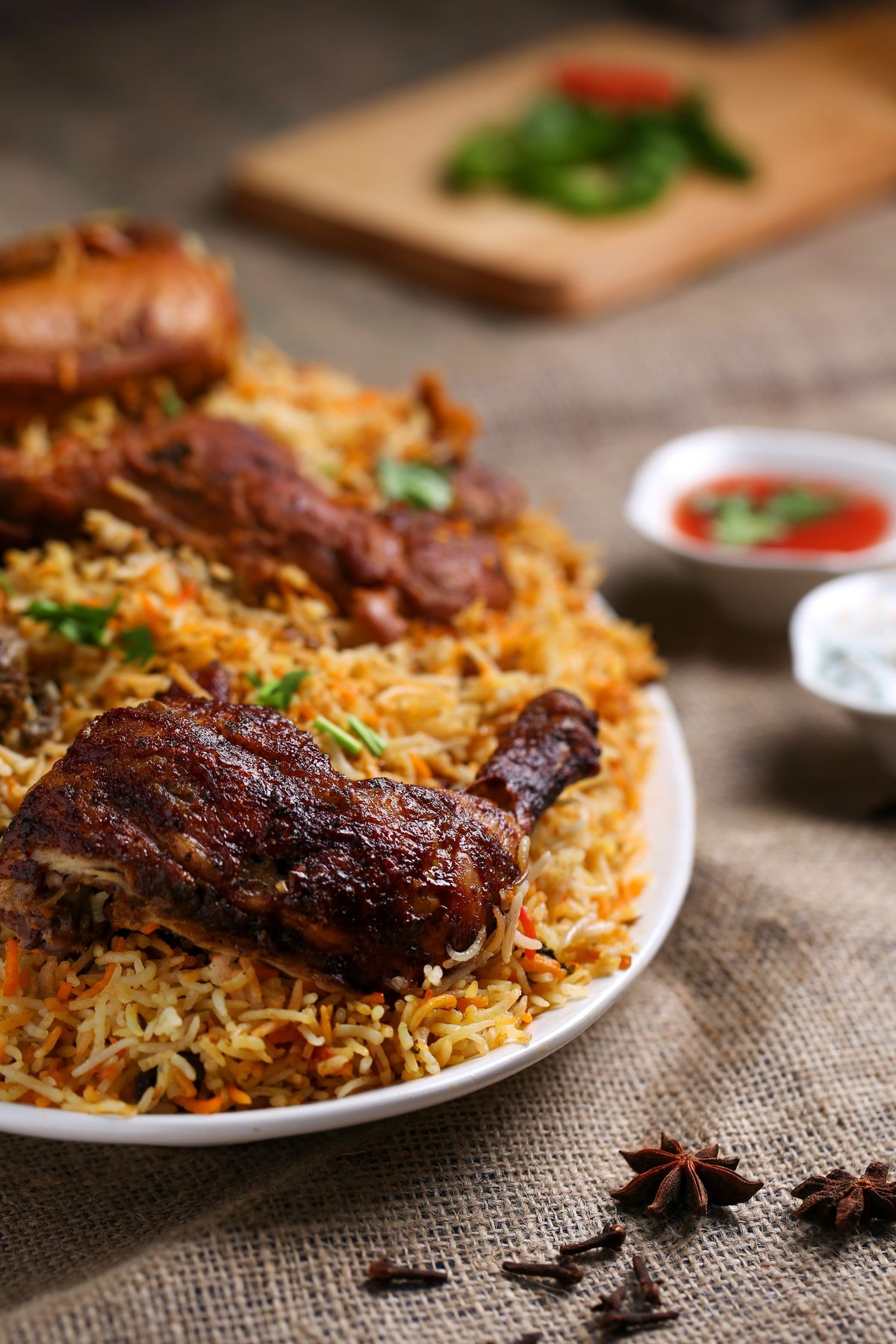 Chicken biryani on a plate with raita and a red chutney.
