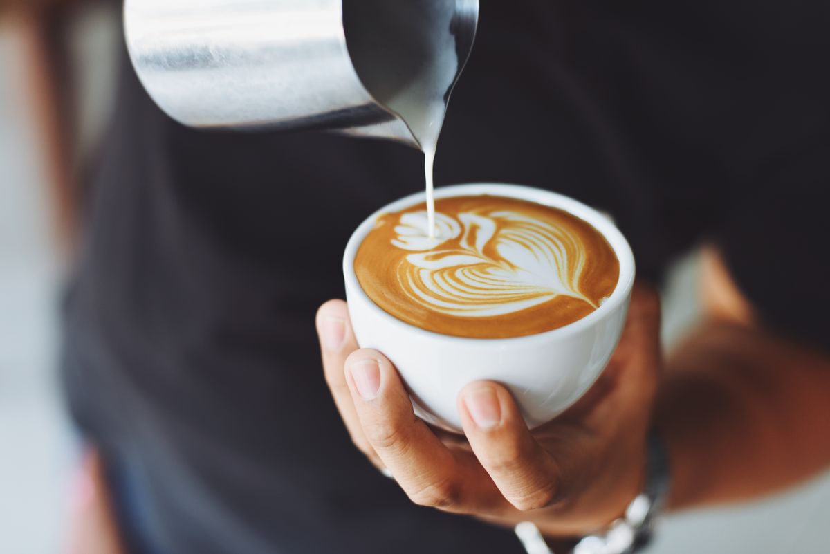 A barista pouring latte art into a cup of coffee.
