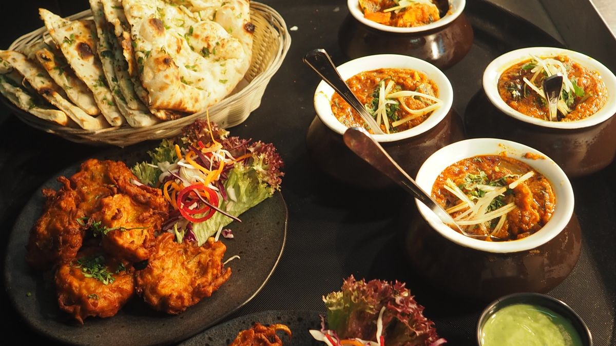 A shared Indian plate of pakora, butter naan, and bowls of gravy.